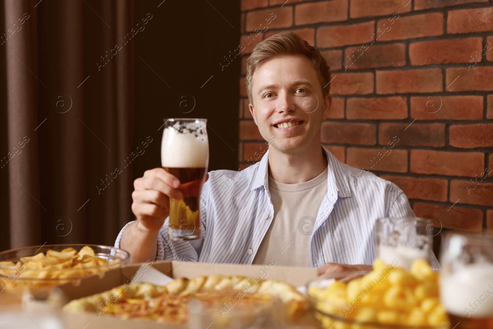 Photo of Young man with glass of beer at table with food in bar