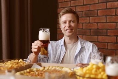 Photo of Young man with glass of beer at table with food in bar