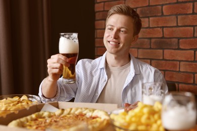 Photo of Young man with glass of beer at table with food in bar