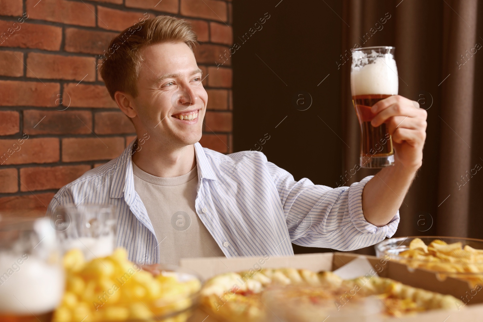 Photo of Young man with glass of beer at table with food in bar
