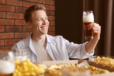 Photo of Young man with glass of beer at table with food in bar