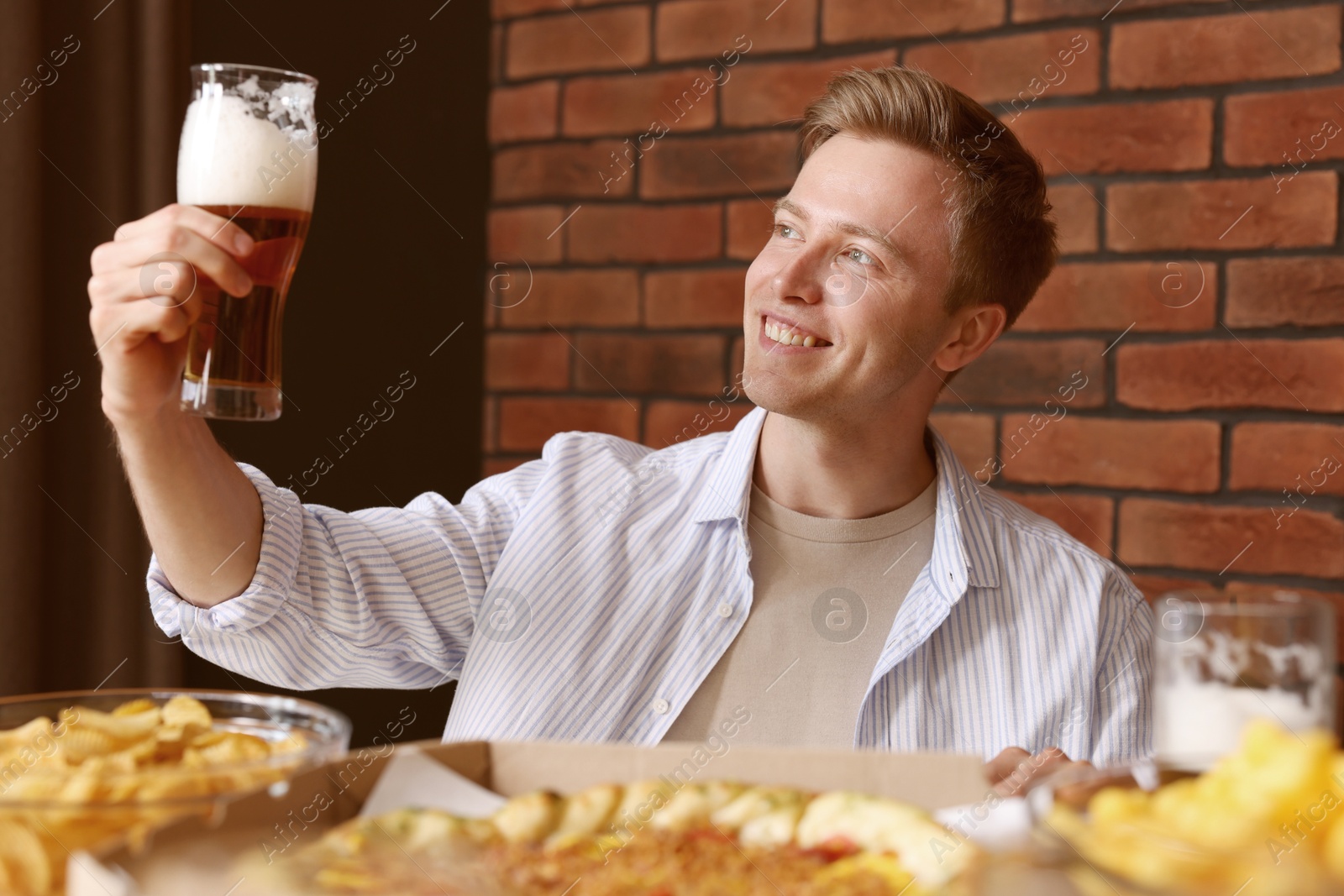 Photo of Young man with glass of beer at table with food in bar