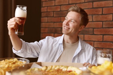 Photo of Young man with glass of beer at table with food in bar