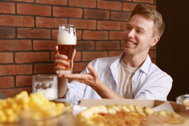 Photo of Young man with glass of beer at table with food in bar