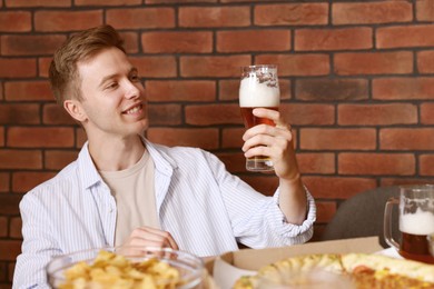 Photo of Young man with glass of beer at table with food in bar