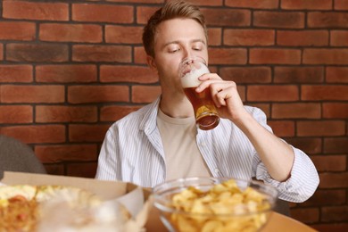 Photo of Young man drinking beer at table with food in bar