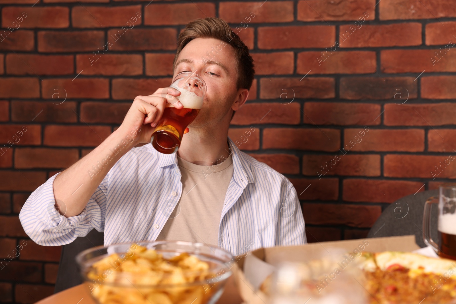 Photo of Young man drinking beer at table with food in bar