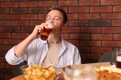 Photo of Young man drinking beer at table with food in bar
