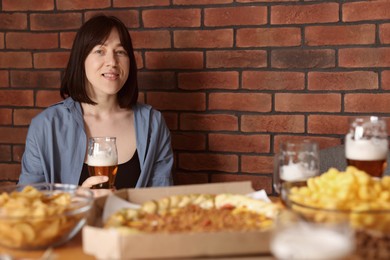 Photo of Young woman with glass of beer at table with food in bar