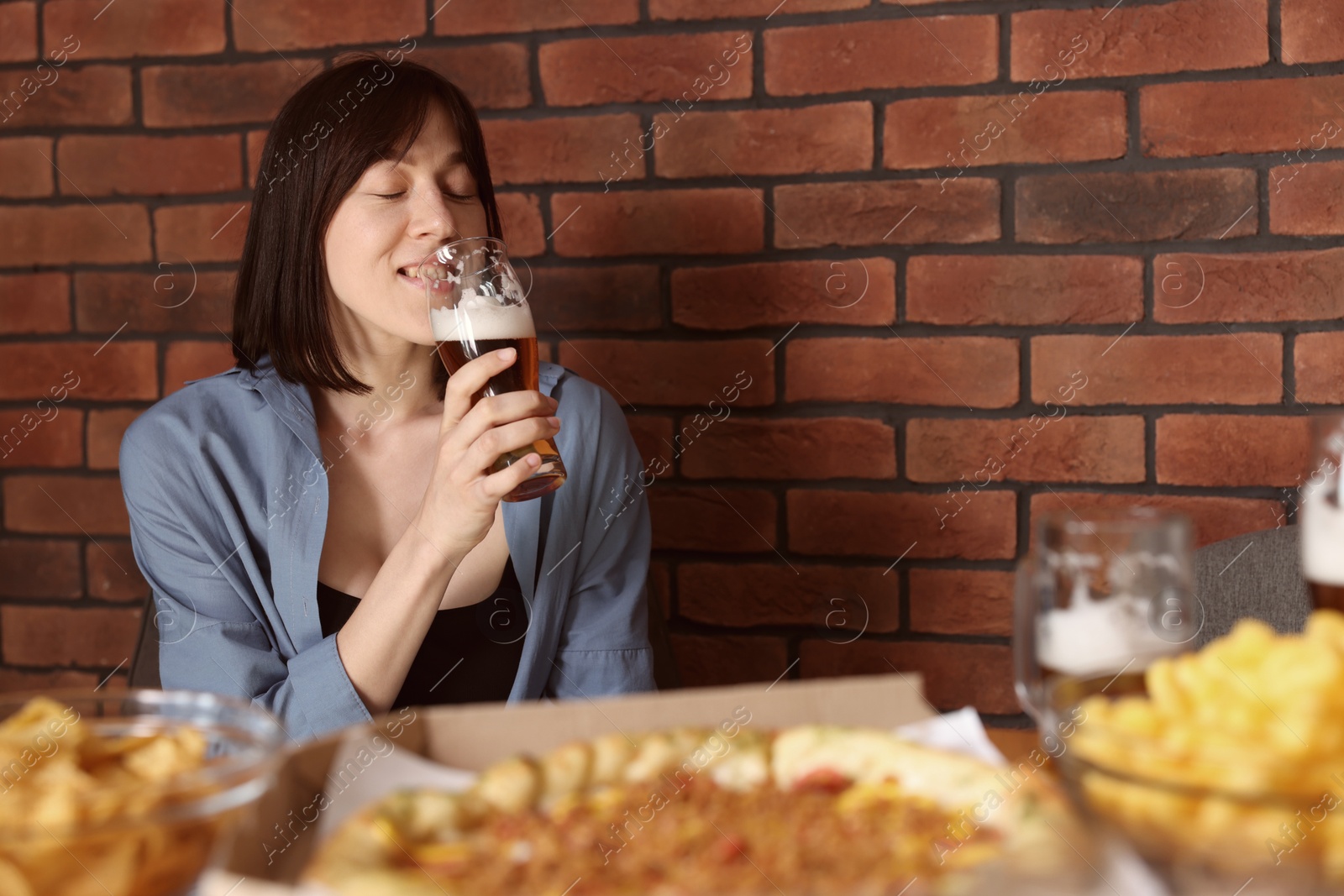 Photo of Young woman drinking beer at table with food in bar
