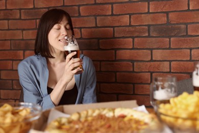 Photo of Young woman drinking beer at table with food in bar