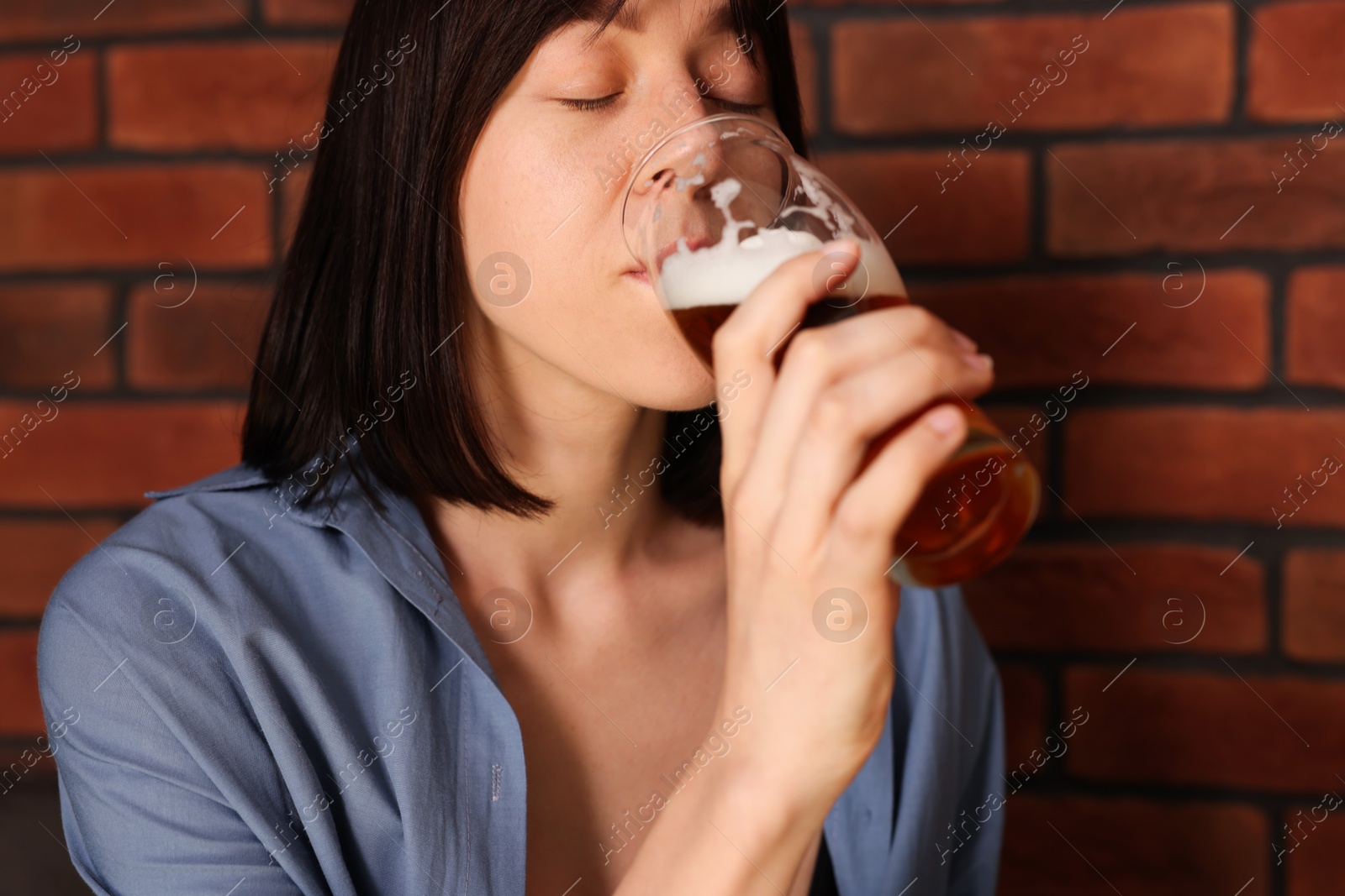 Photo of Young woman drinking beer near brick wall in bar