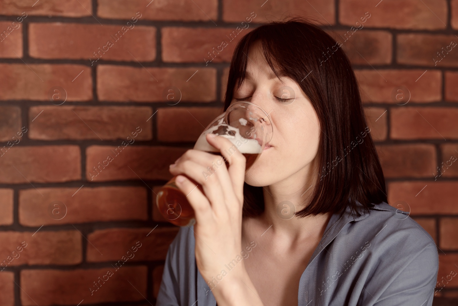 Photo of Young woman drinking beer near brick wall in bar