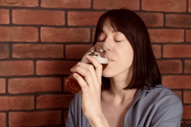 Photo of Young woman drinking beer near brick wall in bar