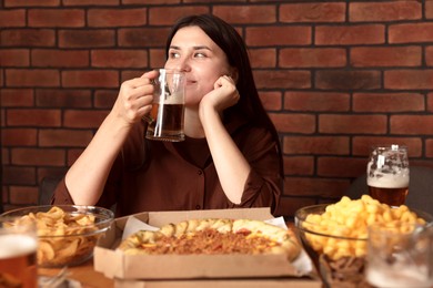 Photo of Young woman drinking beer at table with food in bar