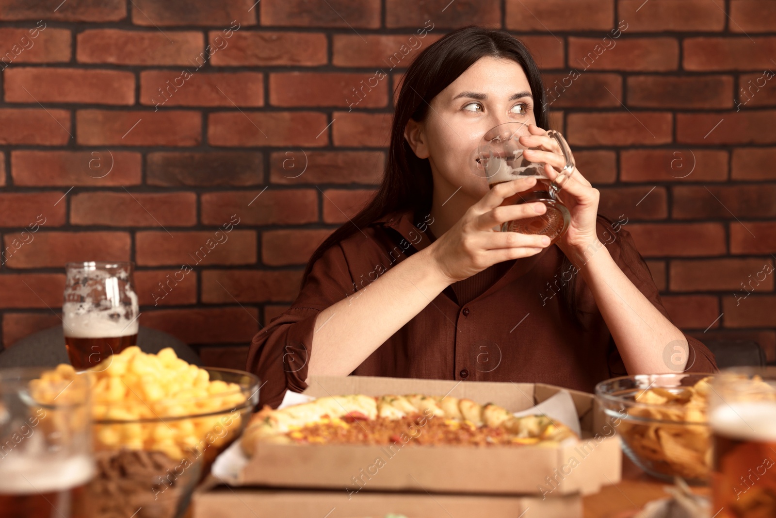Photo of Young woman drinking beer at table with food in bar