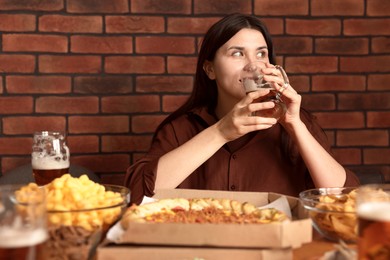 Photo of Young woman drinking beer at table with food in bar