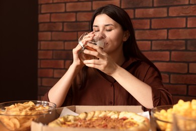Photo of Young woman drinking beer at table with food in bar