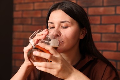 Photo of Young woman drinking beer near brick wall in bar