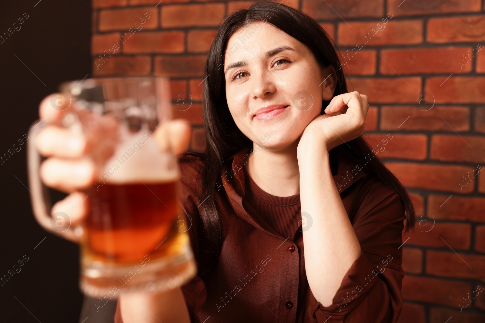 Photo of Young woman with glass of beer near brick wall in bar, selective focus