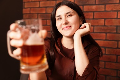 Photo of Young woman with glass of beer near brick wall in bar, selective focus