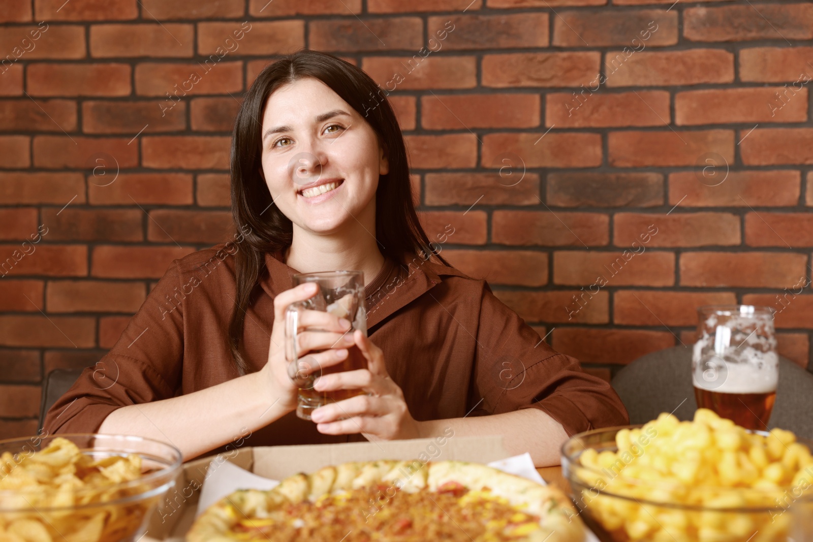 Photo of Young woman with glass of beer at table with food in bar