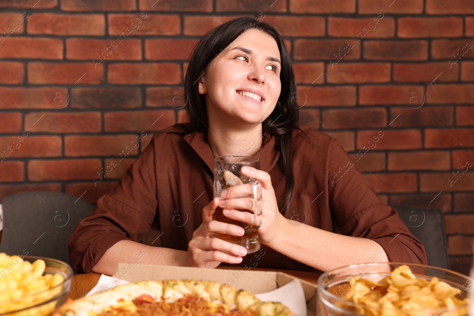 Photo of Young woman with glass of beer at table with food in bar