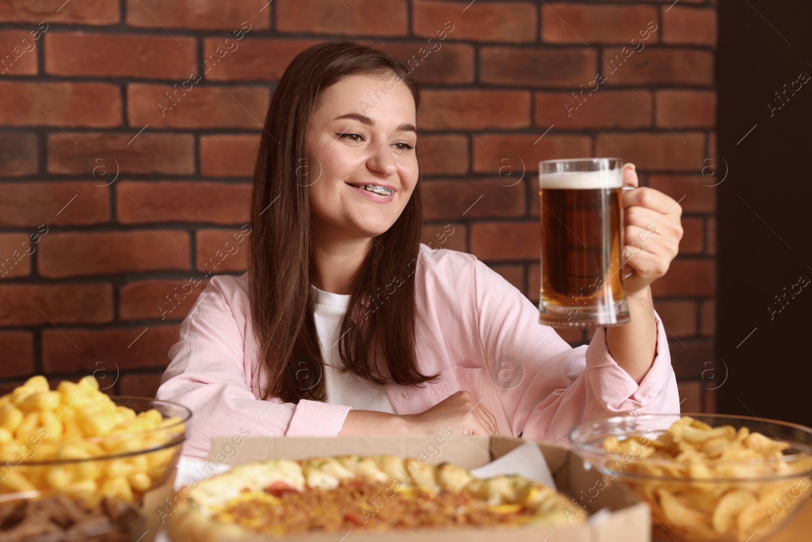 Photo of Young woman with glass of beer at table with food in bar