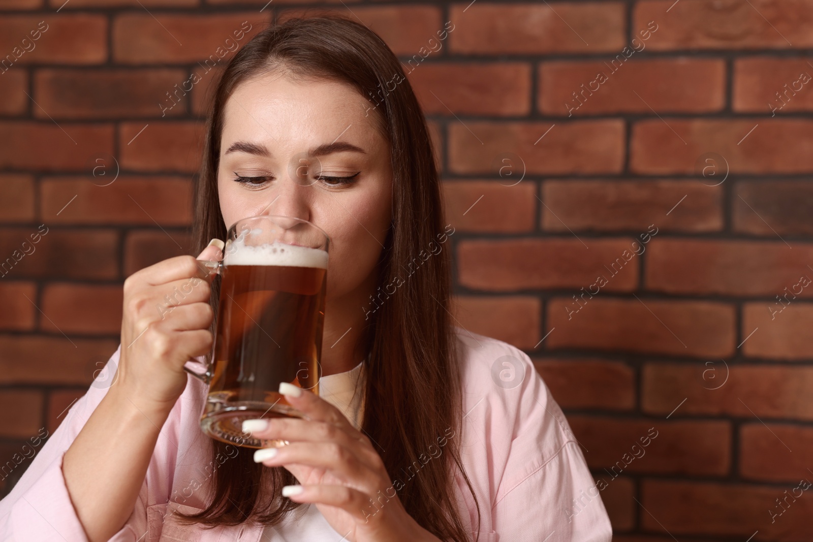Photo of Young woman drinking beer near brick wall in bar