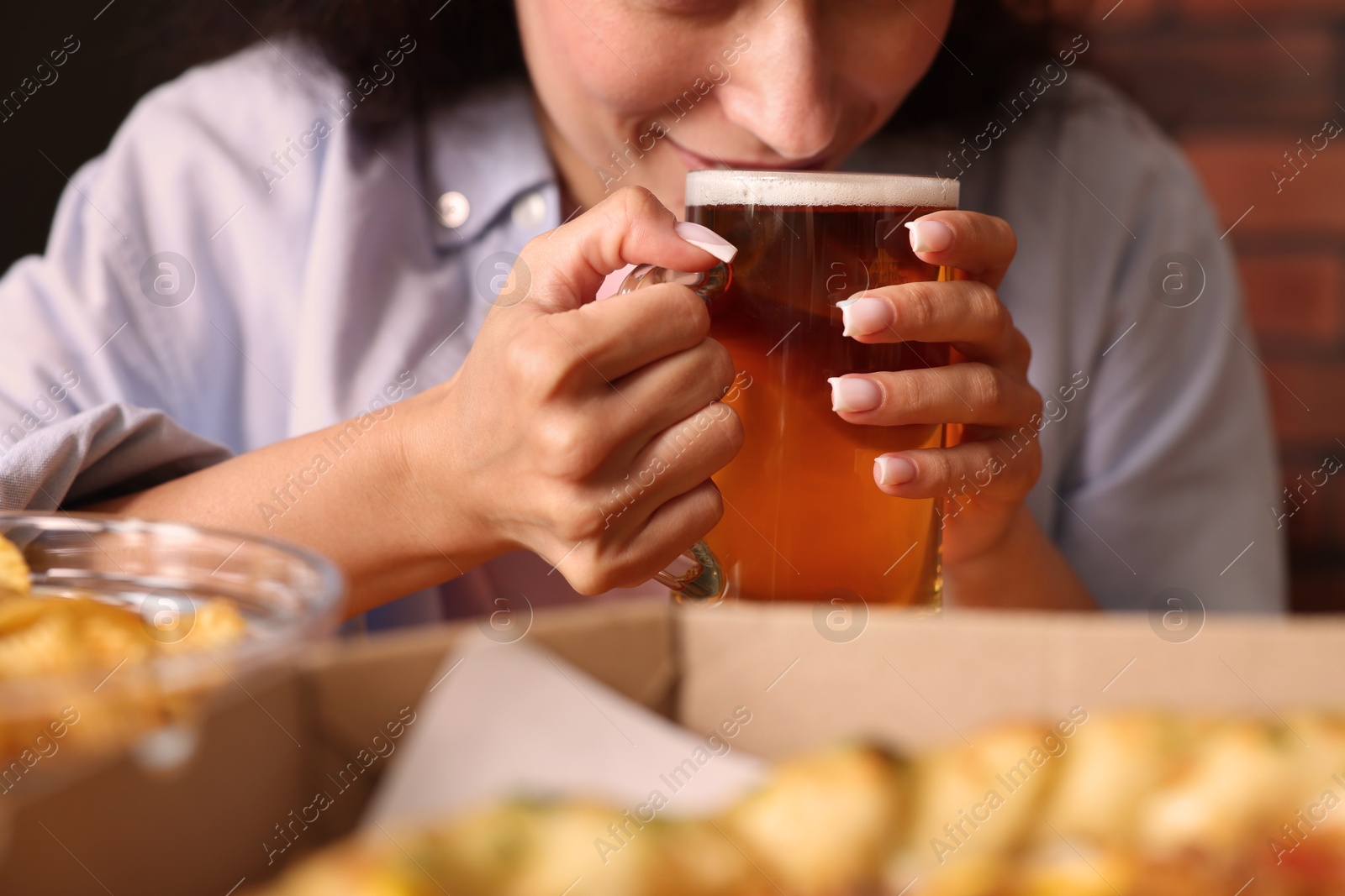 Photo of Young woman drinking beer at table with food in bar, closeup