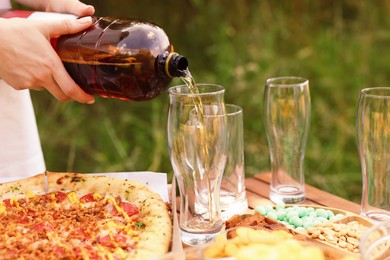 Photo of Woman pouring beer into glass at wooden table with food outdoors, closeup