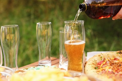 Photo of Woman pouring beer into glass at wooden table with food outdoors, closeup
