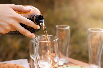 Photo of Woman pouring beer into glass at wooden table with food outdoors, closeup