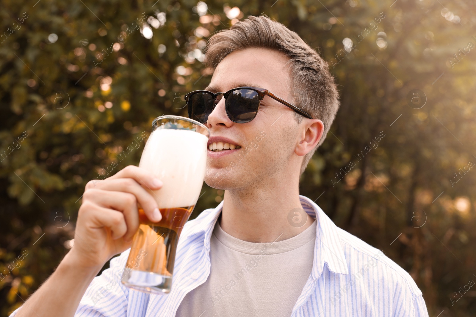 Photo of Young man drinking beer from glass outdoors