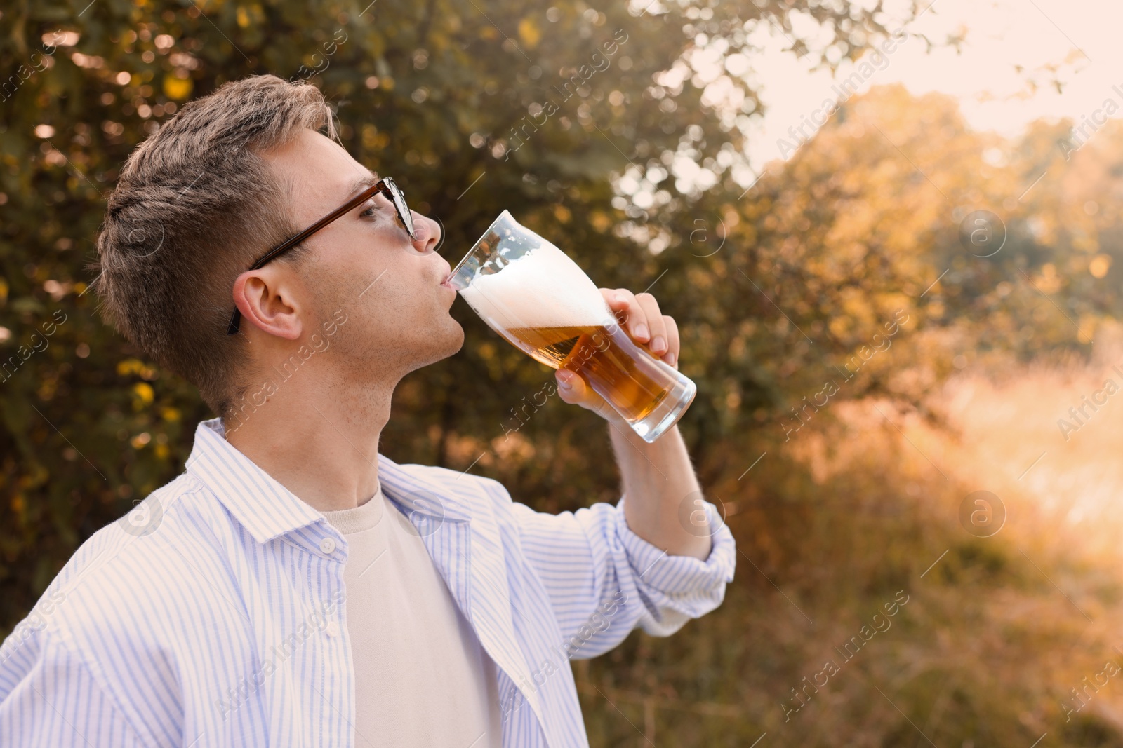 Photo of Young man drinking beer from glass outdoors, space for text