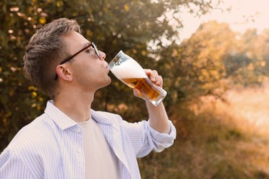 Photo of Young man drinking beer from glass outdoors, space for text
