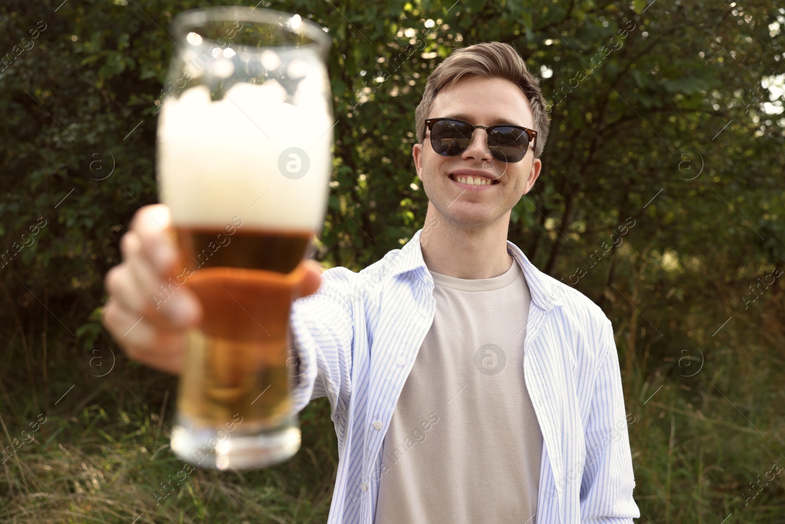 Photo of Young man with glass of beer outdoors, selective focus