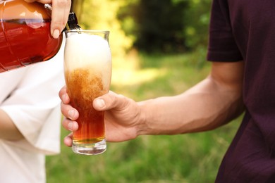 Photo of Young woman pouring beer into glass outdoors, closeup