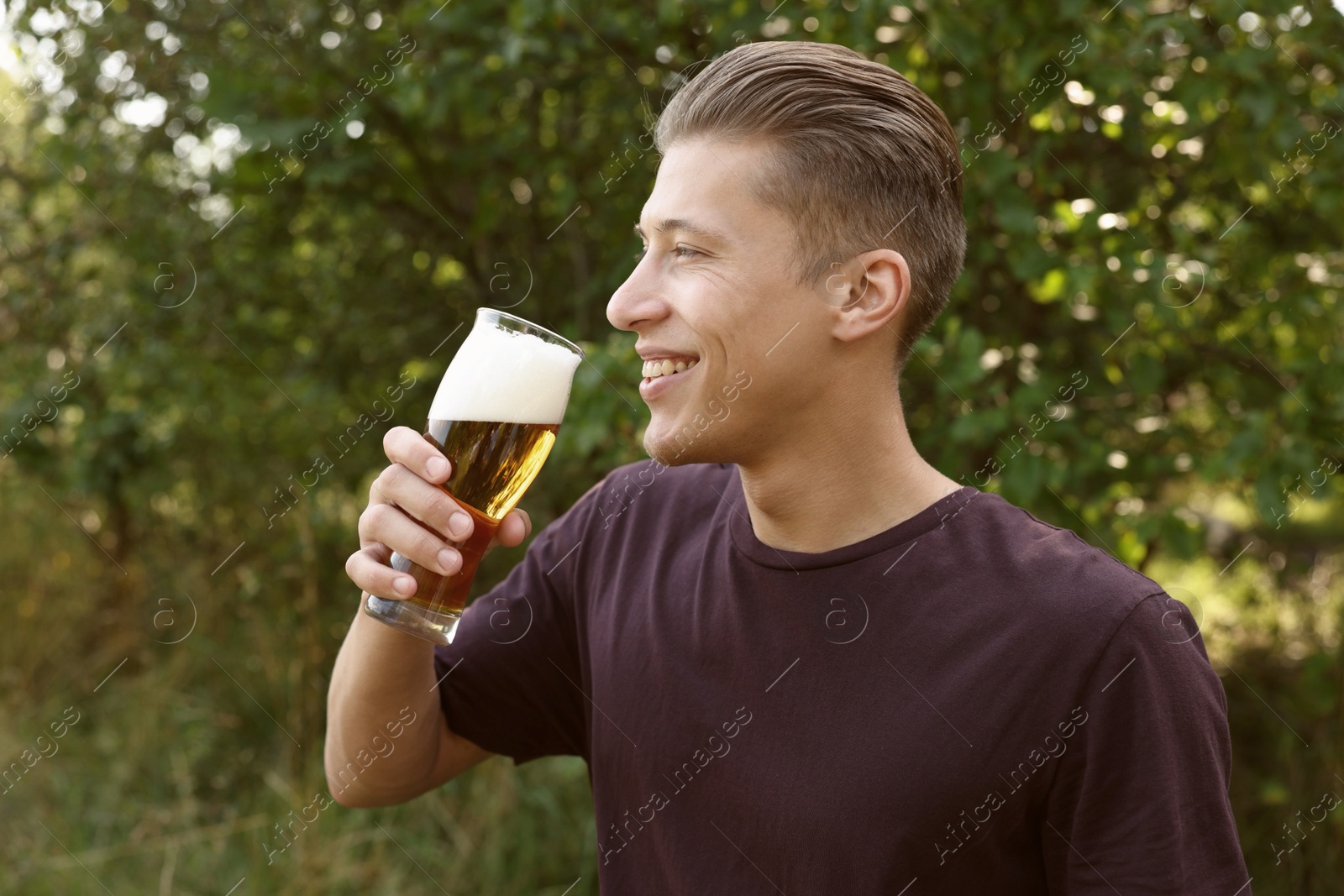 Photo of Young man drinking beer from glass outdoors