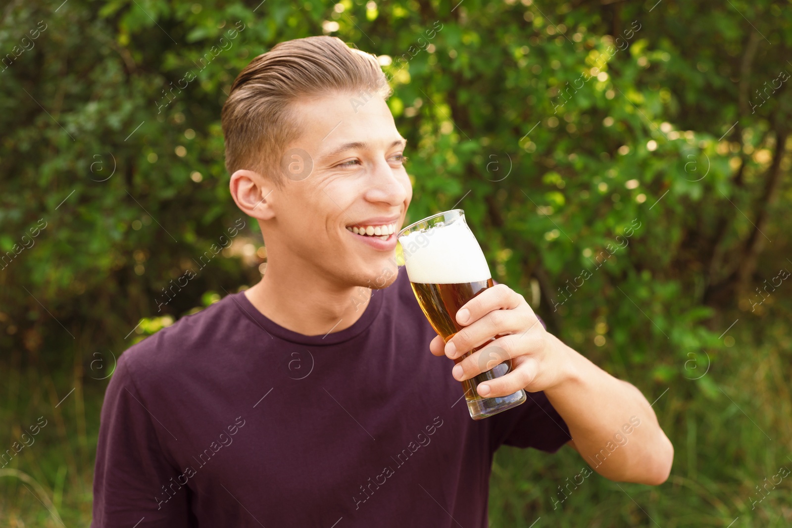 Photo of Young man drinking beer from glass outdoors