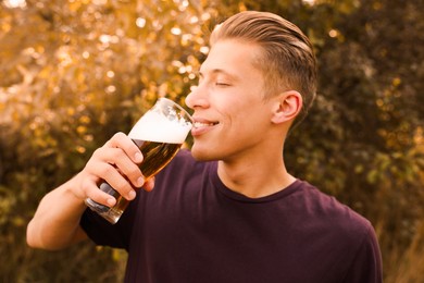 Photo of Young man drinking beer from glass outdoors