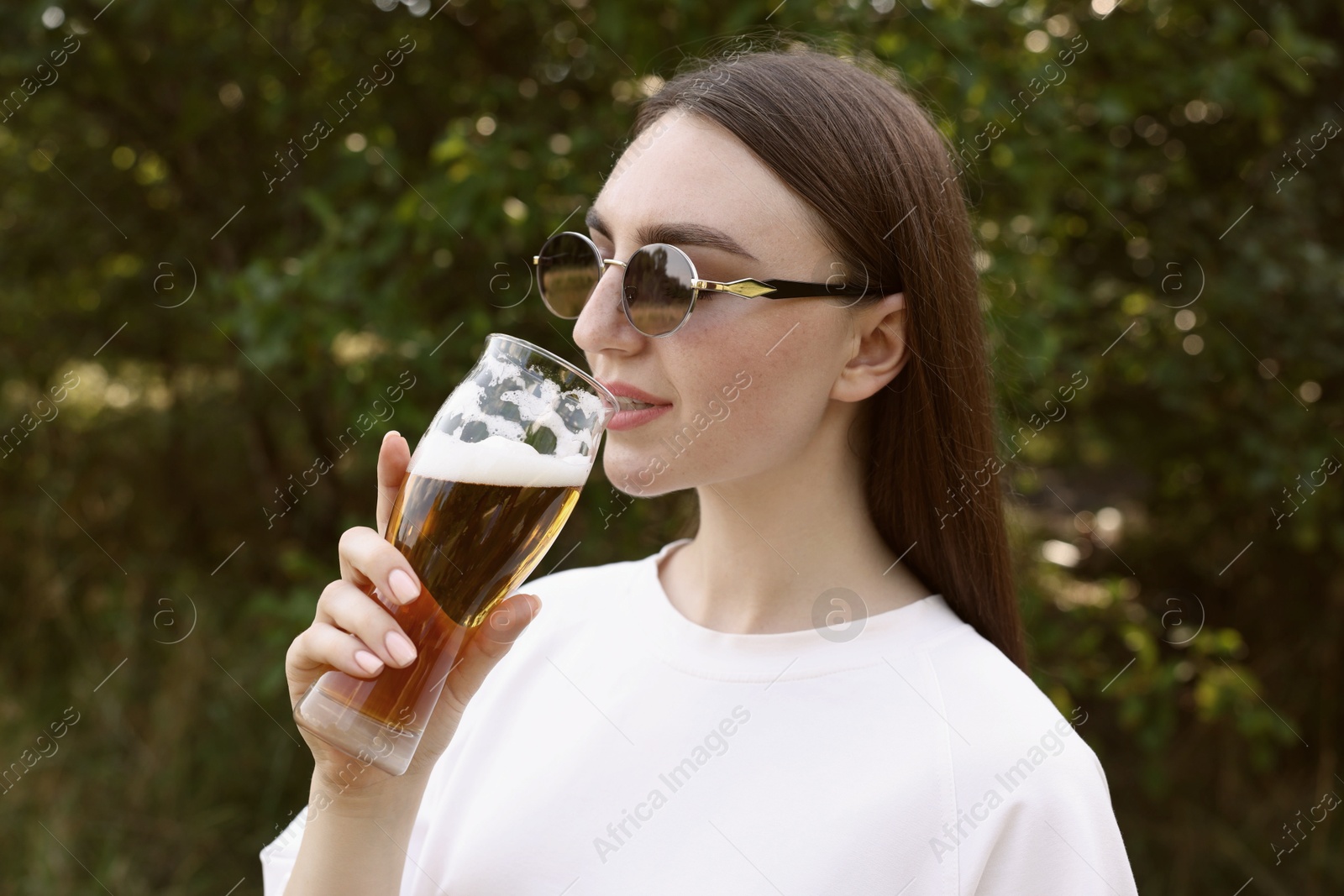 Photo of Young woman drinking beer from glass outdoors