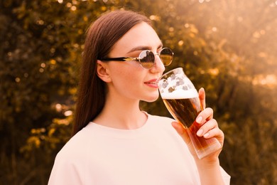 Photo of Young woman drinking beer from glass outdoors