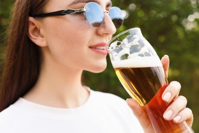 Photo of Young woman drinking beer from glass outdoors, closeup