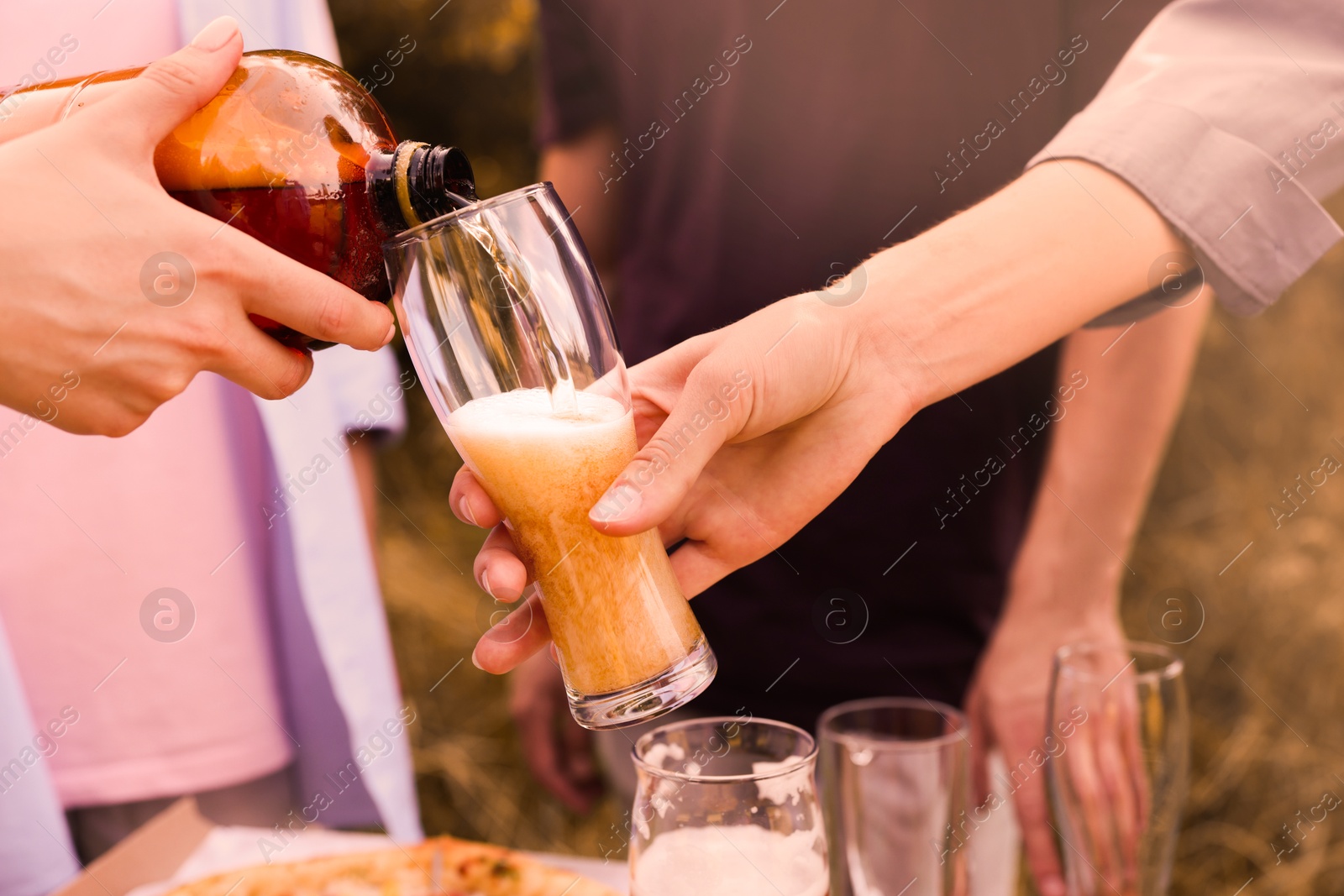 Photo of Young woman pouring beer into glass at table outdoors, closeup