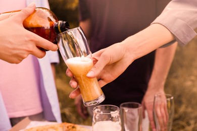 Photo of Young woman pouring beer into glass at table outdoors, closeup