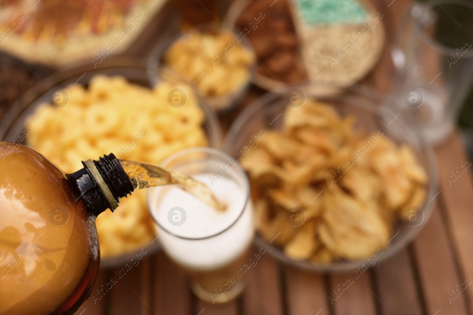 Photo of Pouring beer into glass at wooden table with snacks, above view