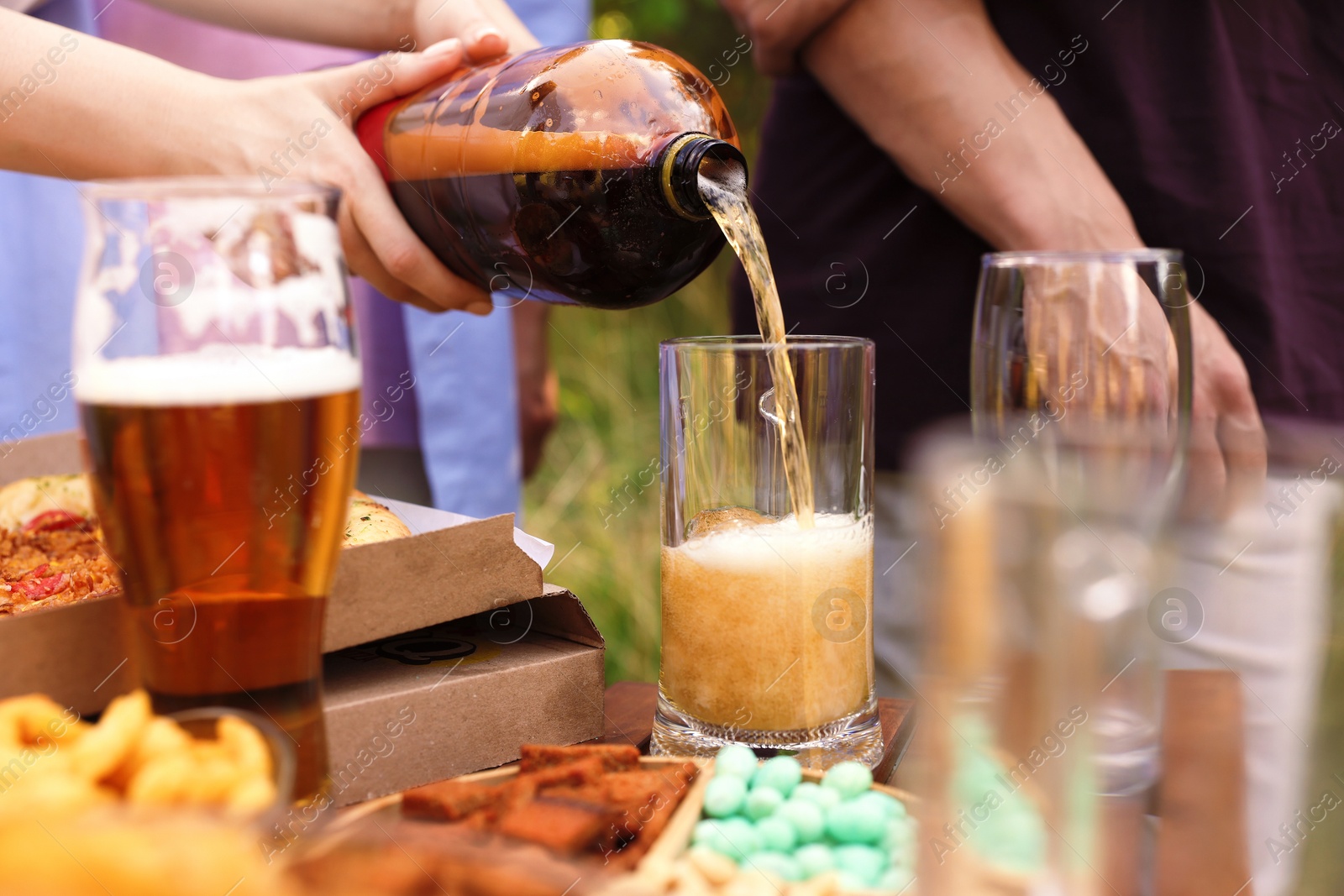Photo of Young woman pouring beer into glass at table outdoors, closeup