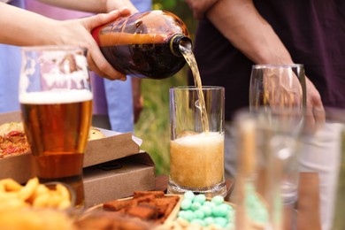 Photo of Young woman pouring beer into glass at table outdoors, closeup