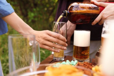 Photo of Young woman pouring beer into glass at table outdoors, closeup
